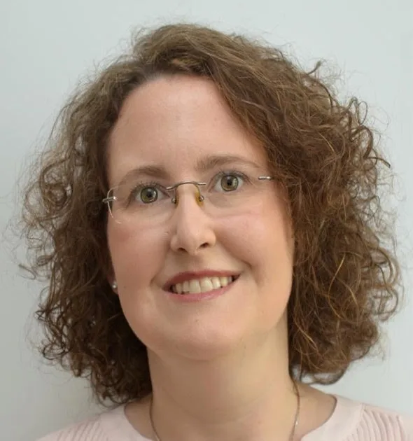 Woman with curly brown hair and glasses smiling at camera in professional headshot