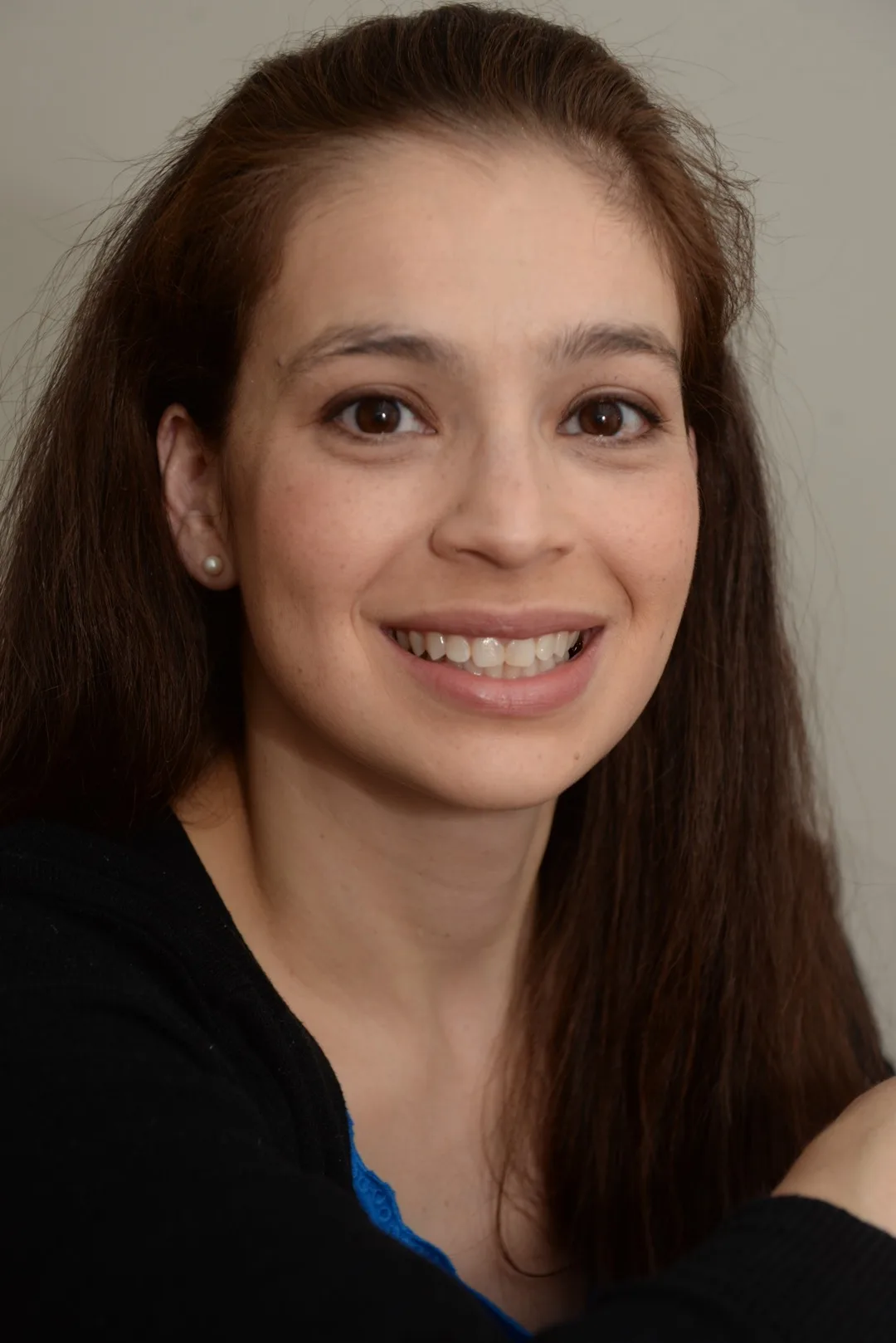 Woman with long brown hair and pearl earrings smiling at camera