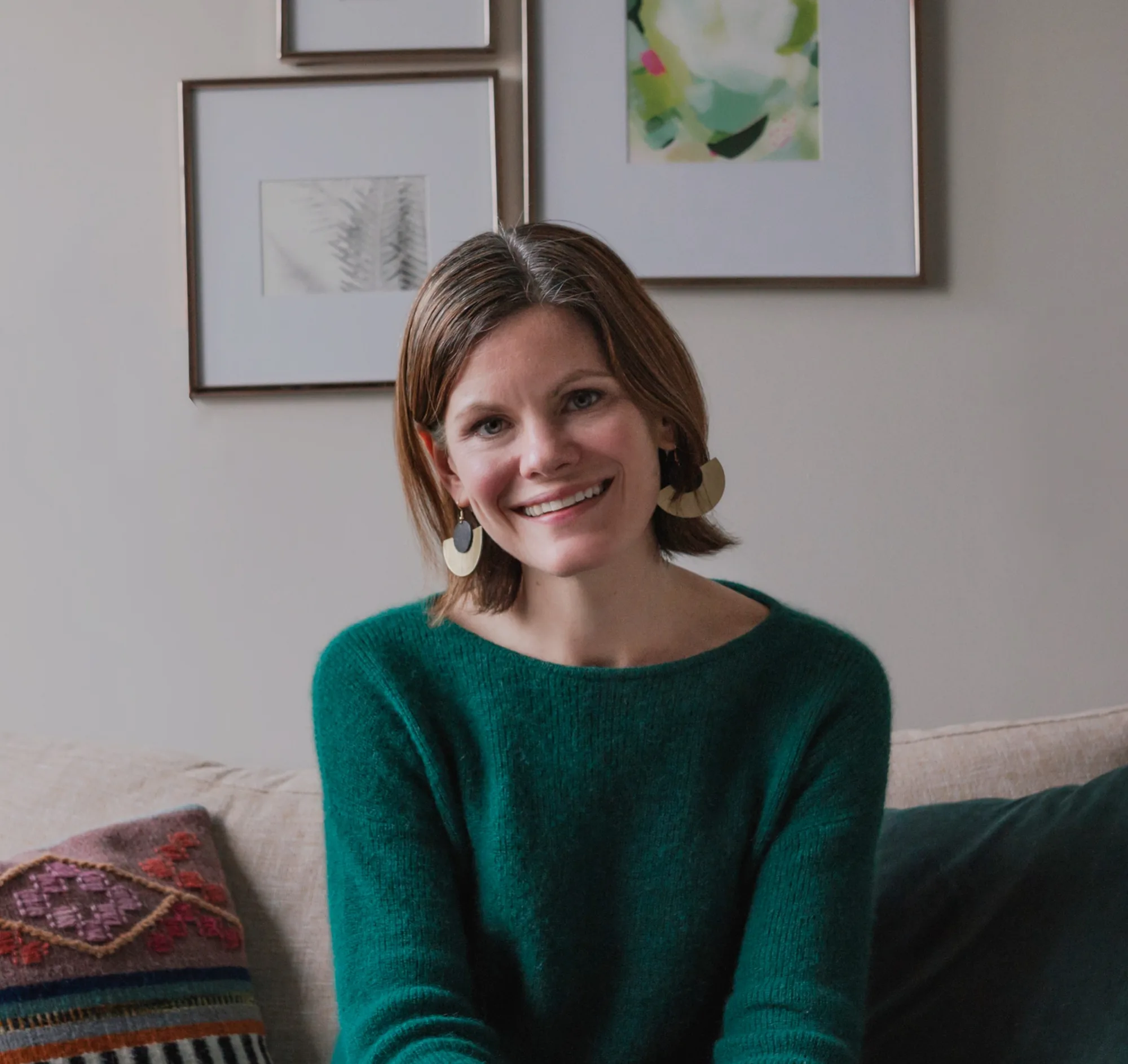 Anne Welsh smiling in green sweater with framed artwork in background
