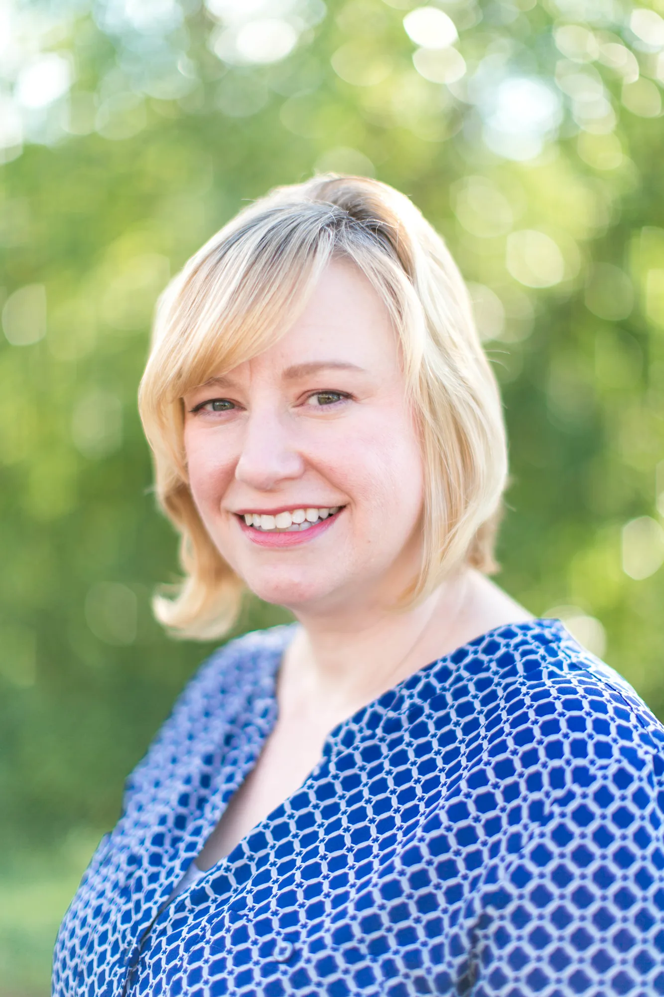 Woman with blonde bob haircut smiling in blue patterned top outdoors