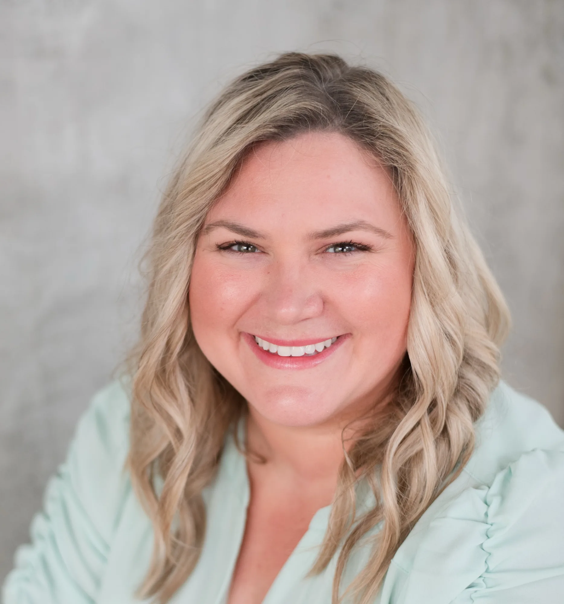 Woman with blonde wavy hair wearing light blue blazer, smiling professional headshot
