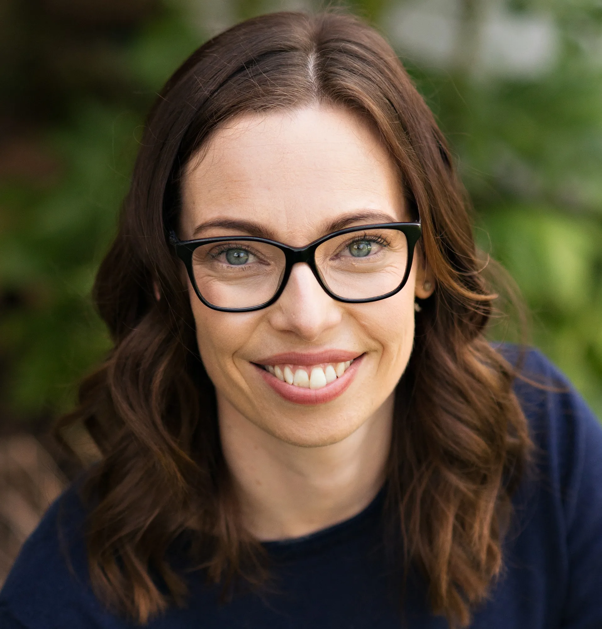 Woman with brown hair and black-framed glasses smiling at camera