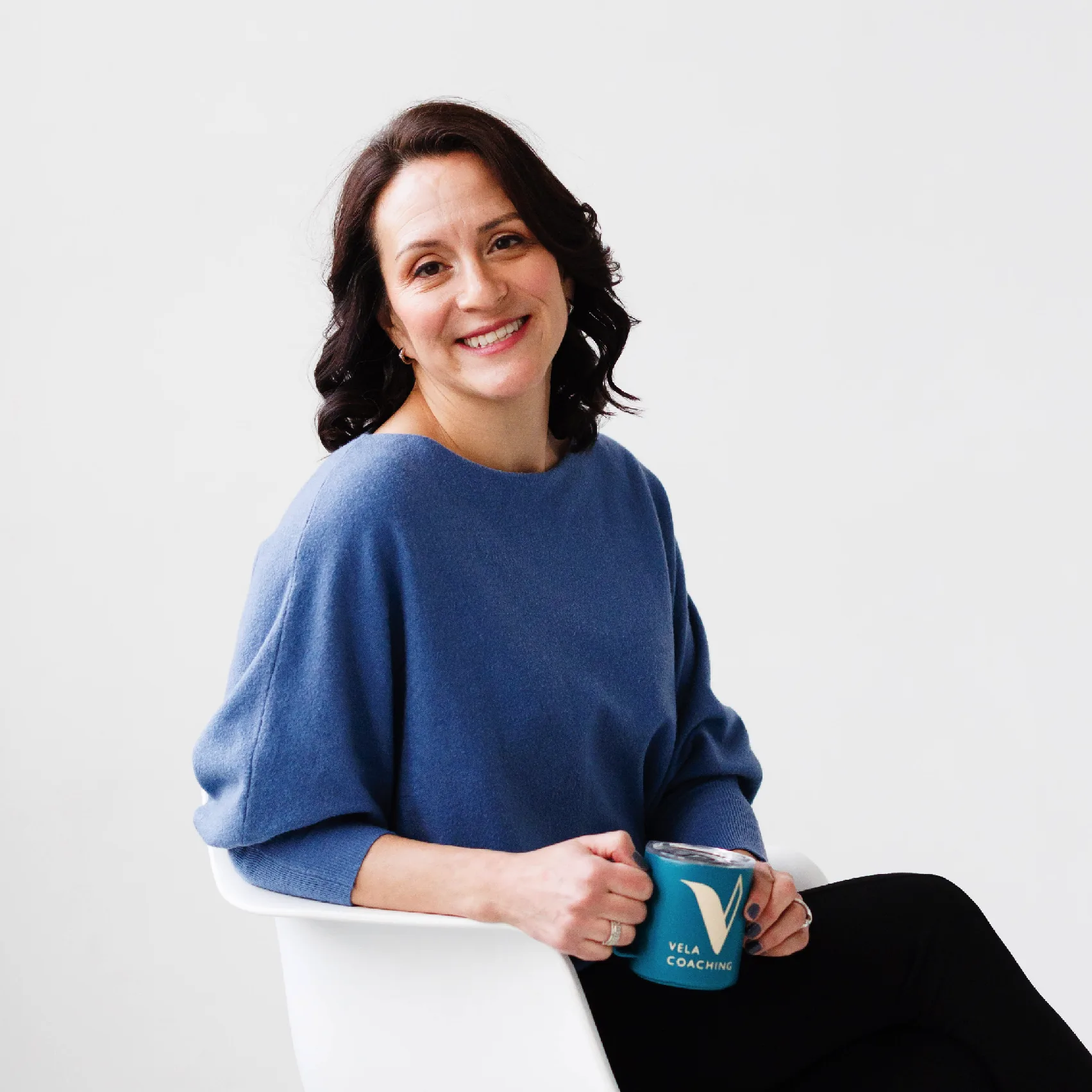Woman in blue sweater smiling and holding Vela Coaching mug