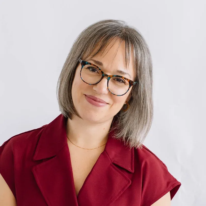 Katelyn Denning smiling in a burgundy dress and tortoiseshell glasses against a white background