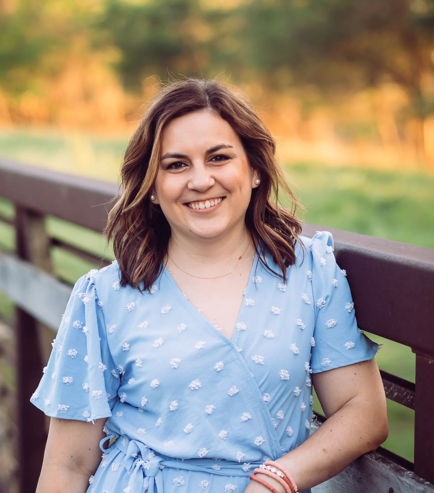 Woman in light blue floral dress smiling while sitting on park bench