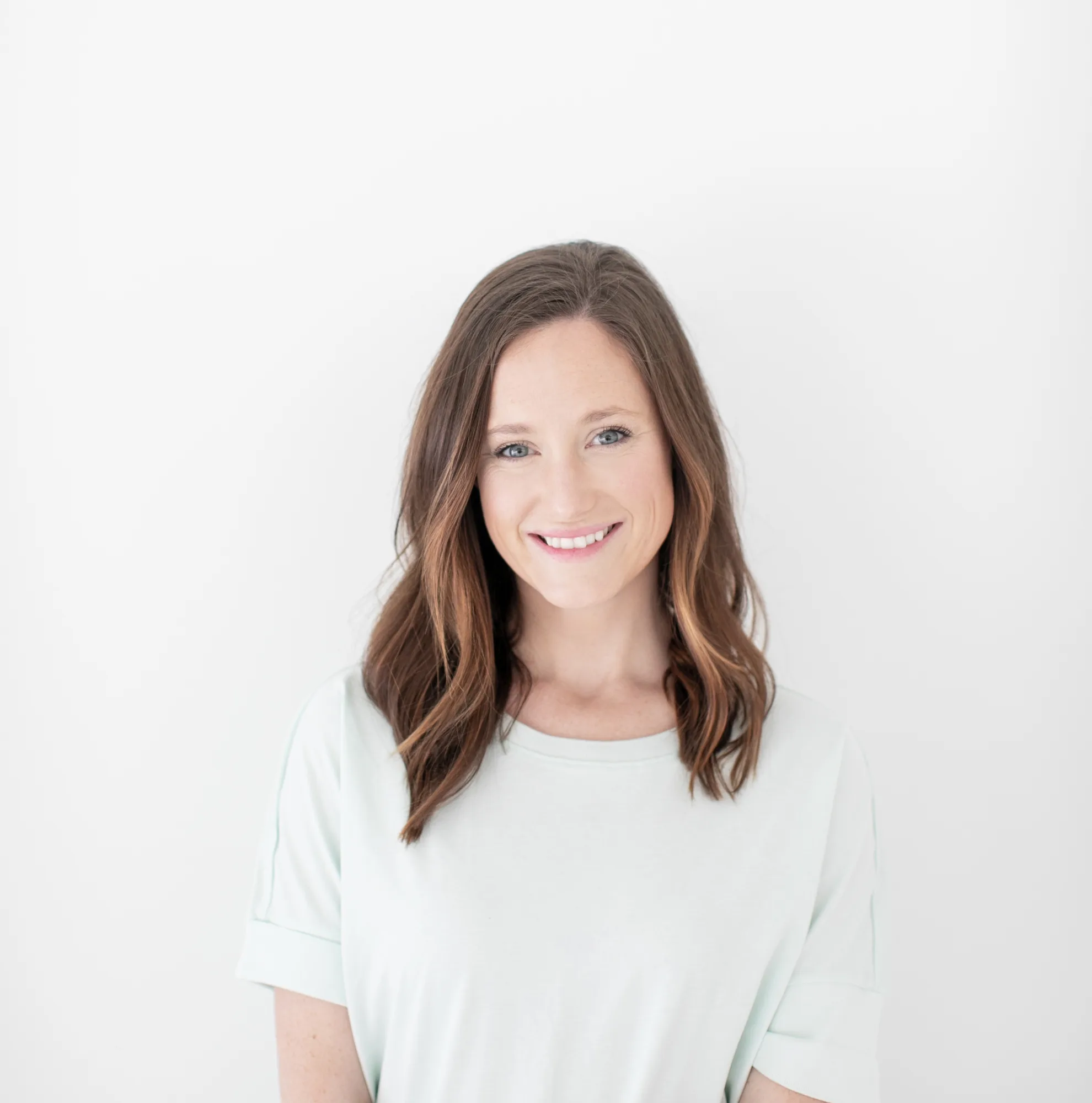 Woman with long brown hair smiling in white shirt against light background
