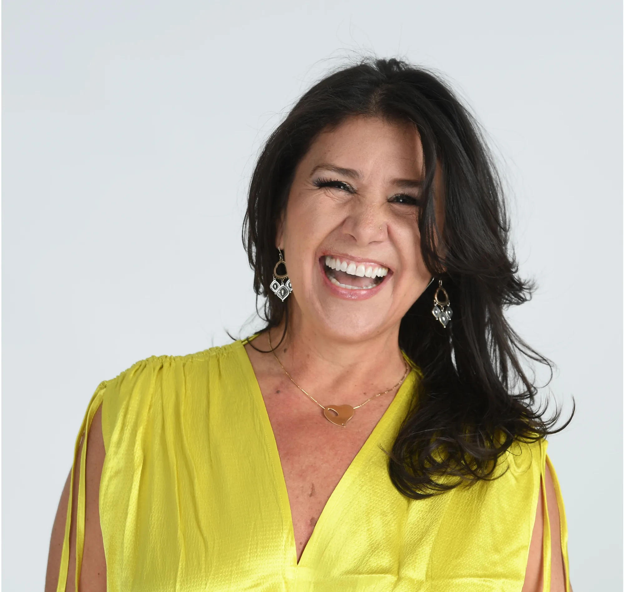 Woman with dark hair wearing a bright yellow dress, smiling against white background