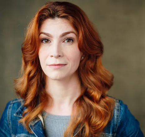 Woman with red wavy hair wearing denim jacket and gray shirt