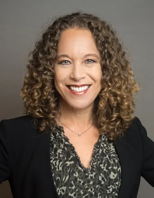 Maxine Pressler smiling in a black blazer against a gray background