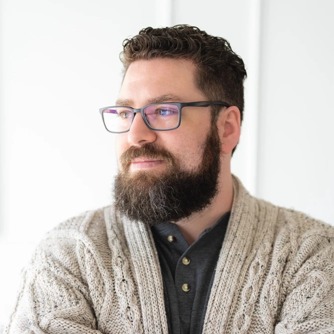 Man with beard and glasses wearing beige cardigan over black shirt