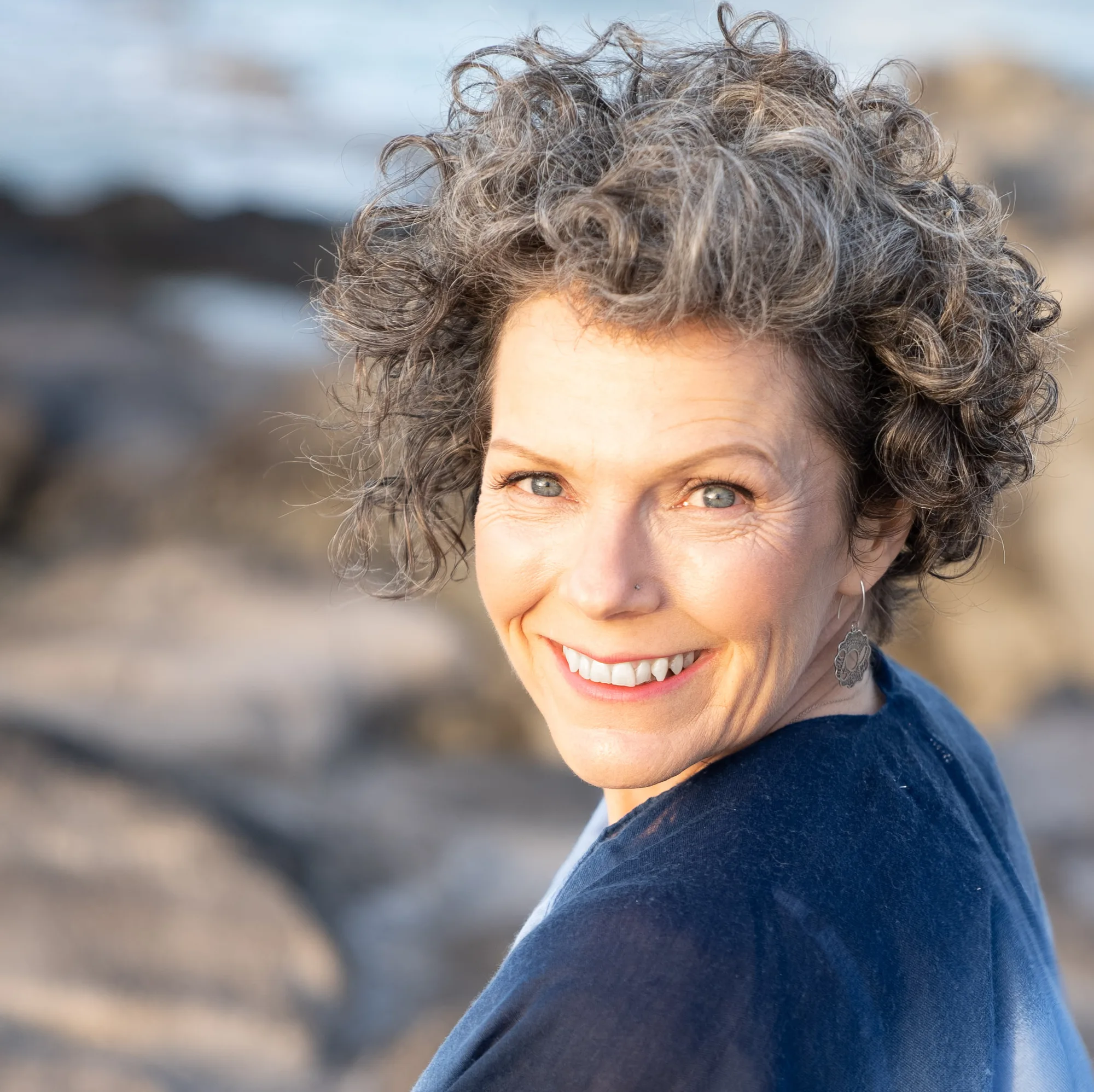 Woman with curly gray hair smiling outdoors wearing navy blue top