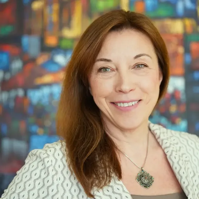 Oxana Holtmann smiling in a cream patterned jacket in front of a colorful painting