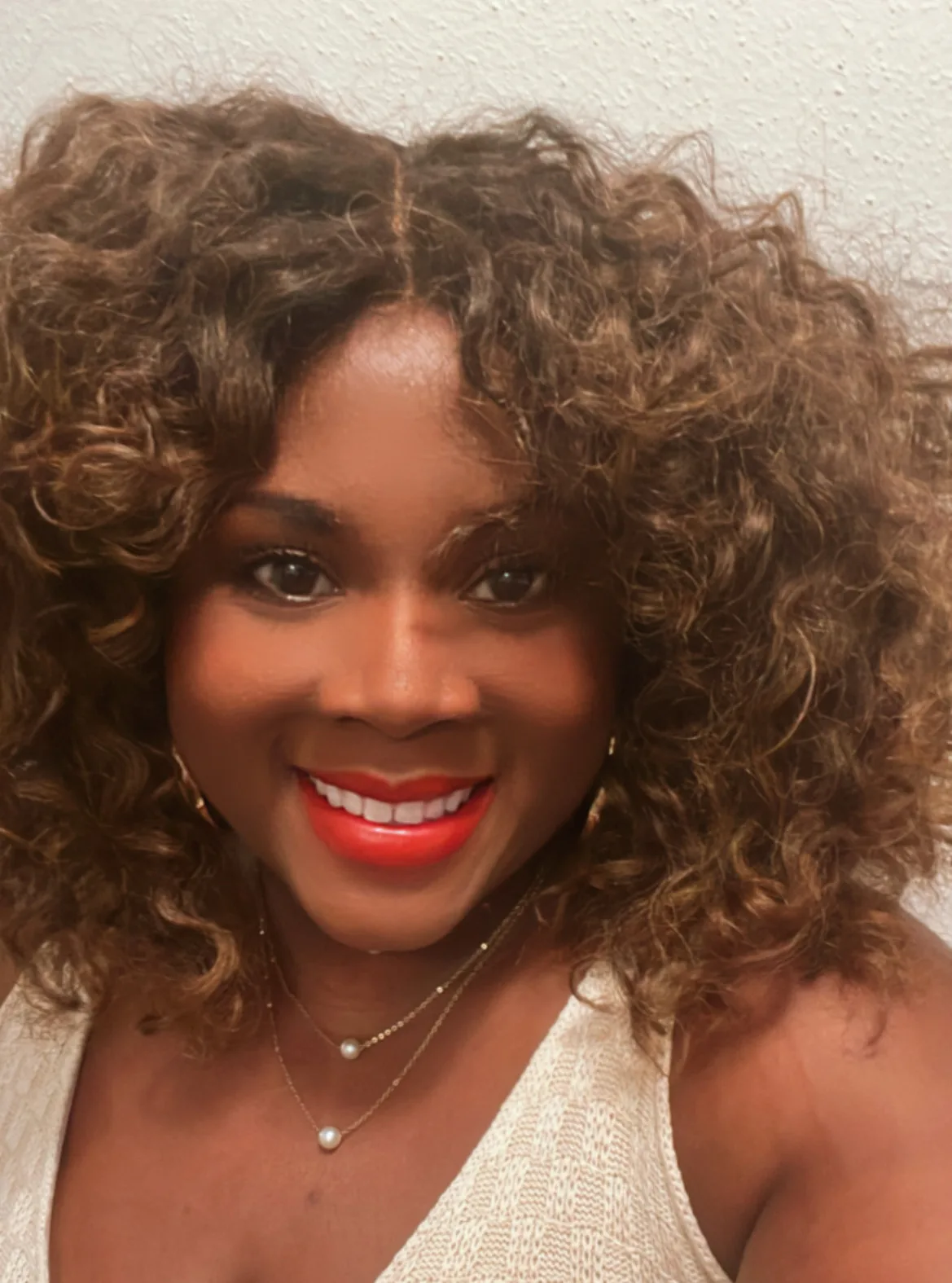 Woman with curly brown hair wearing pearl necklaces and red lipstick smiling