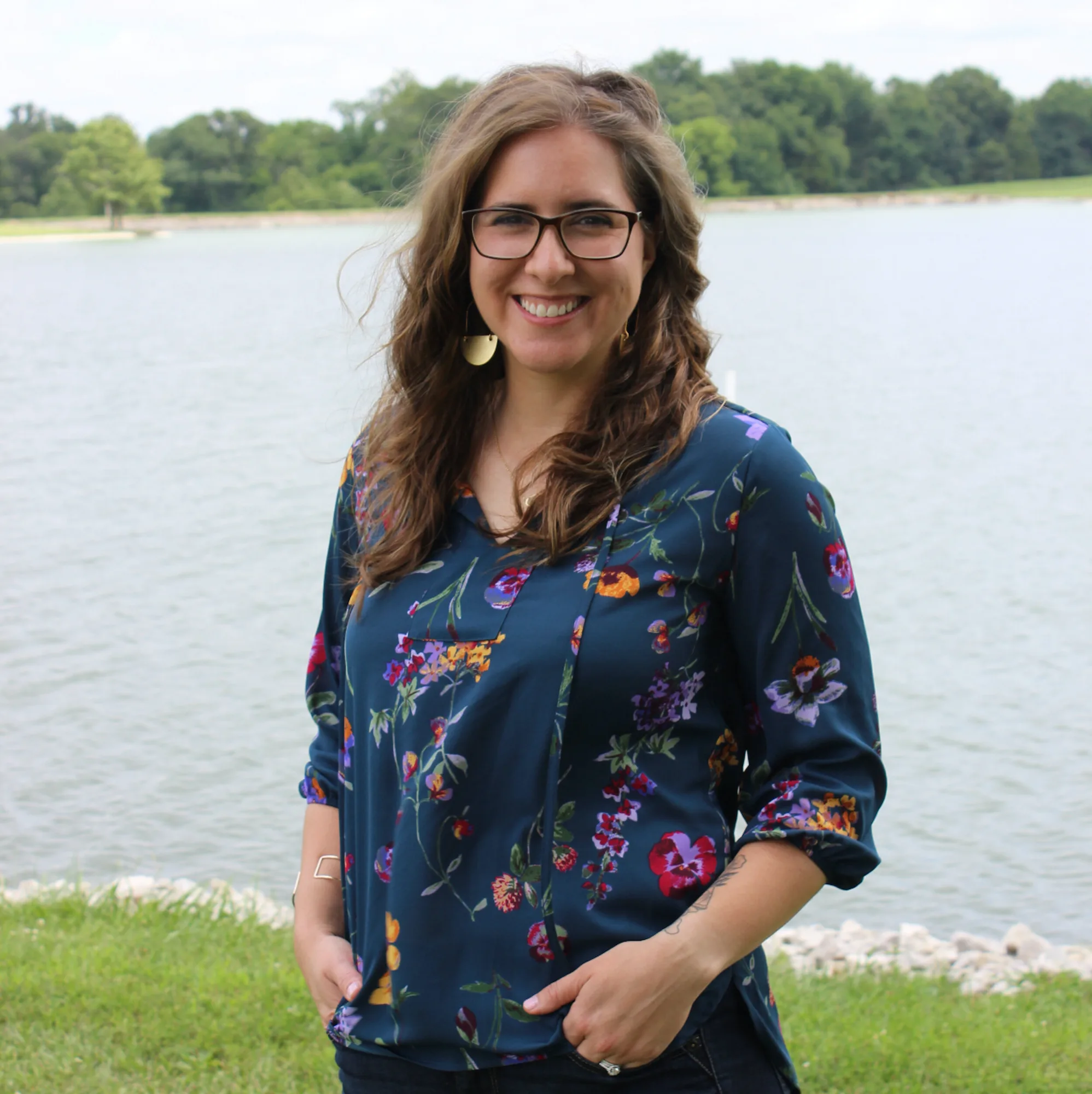 Woman in floral blue blouse and glasses smiling by lake