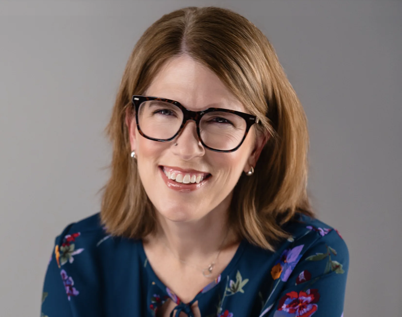 Woman with shoulder-length brown hair, black-framed glasses, and floral top