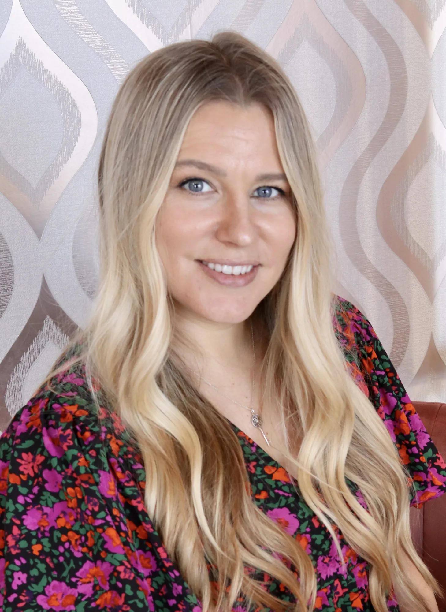 Woman with long blonde hair wearing colorful floral top and necklace