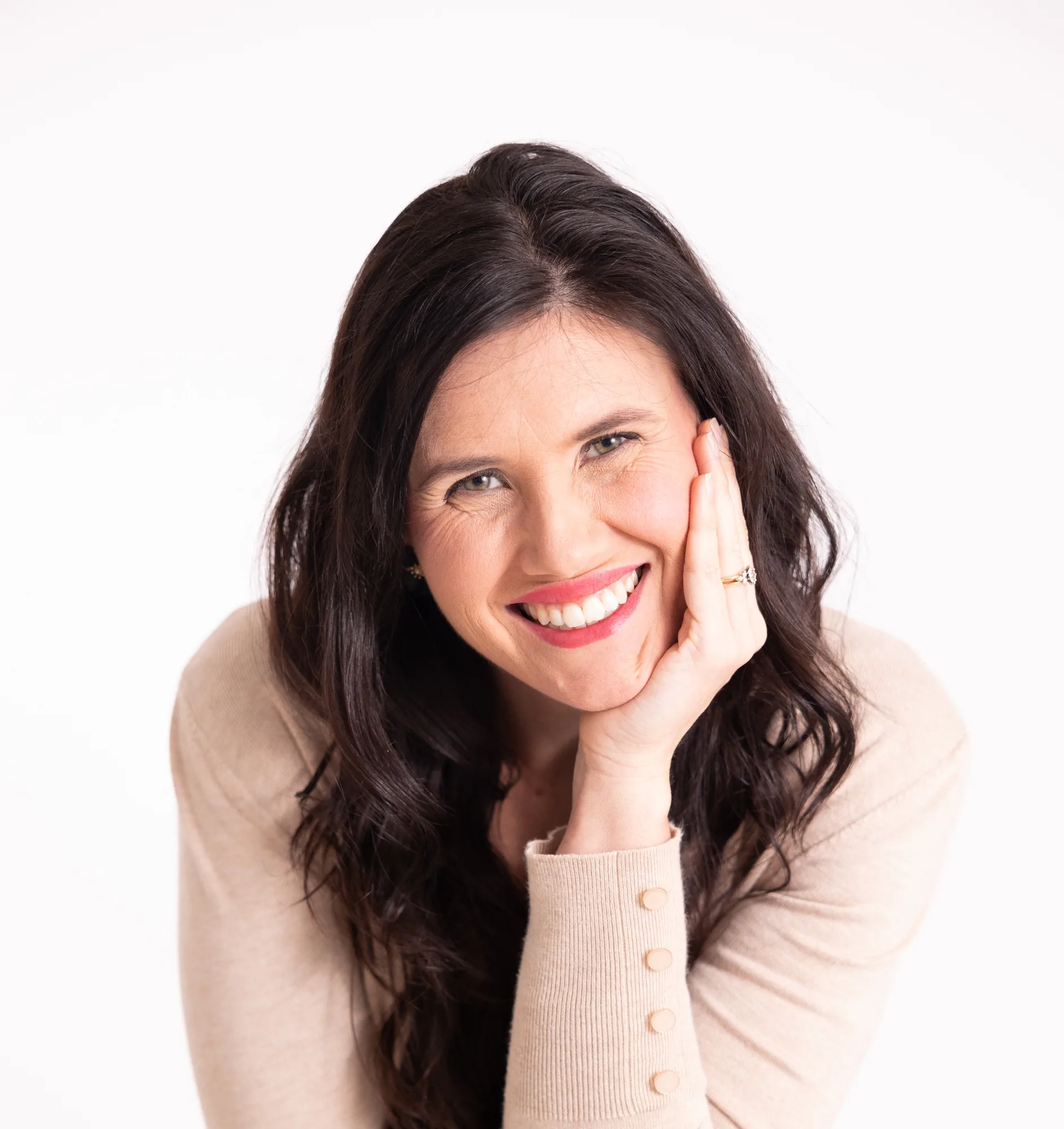 Woman with long dark hair smiling warmly while resting her hand near her face