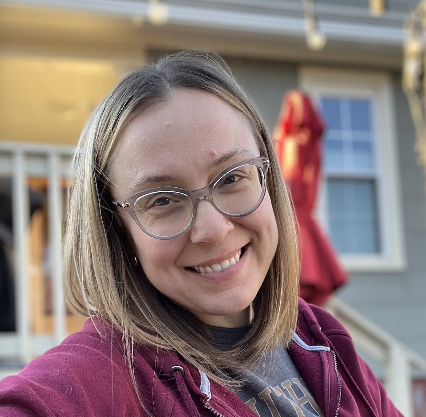 Smiling woman with round glasses wearing a burgundy hoodie outdoors
