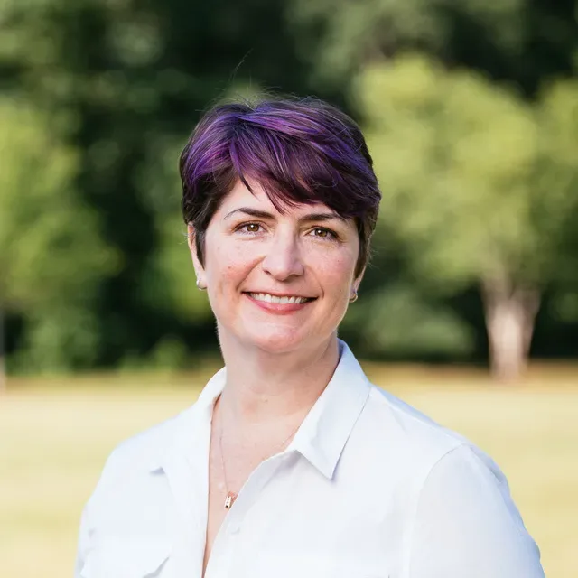 Susannah Baldwin smiling in a white button-up shirt outdoors in front of trees