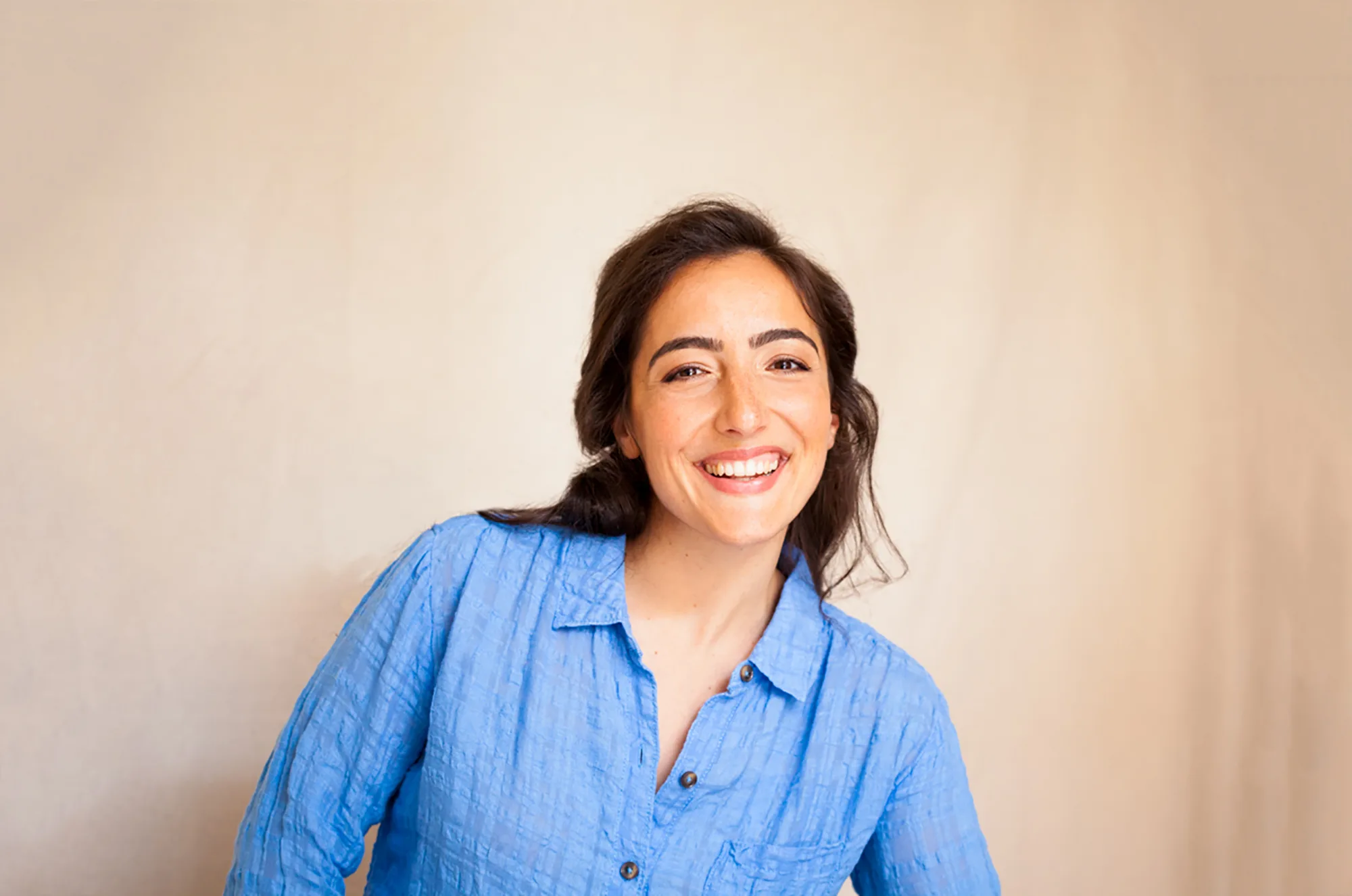 Woman in blue shirt smiling warmly against a beige background