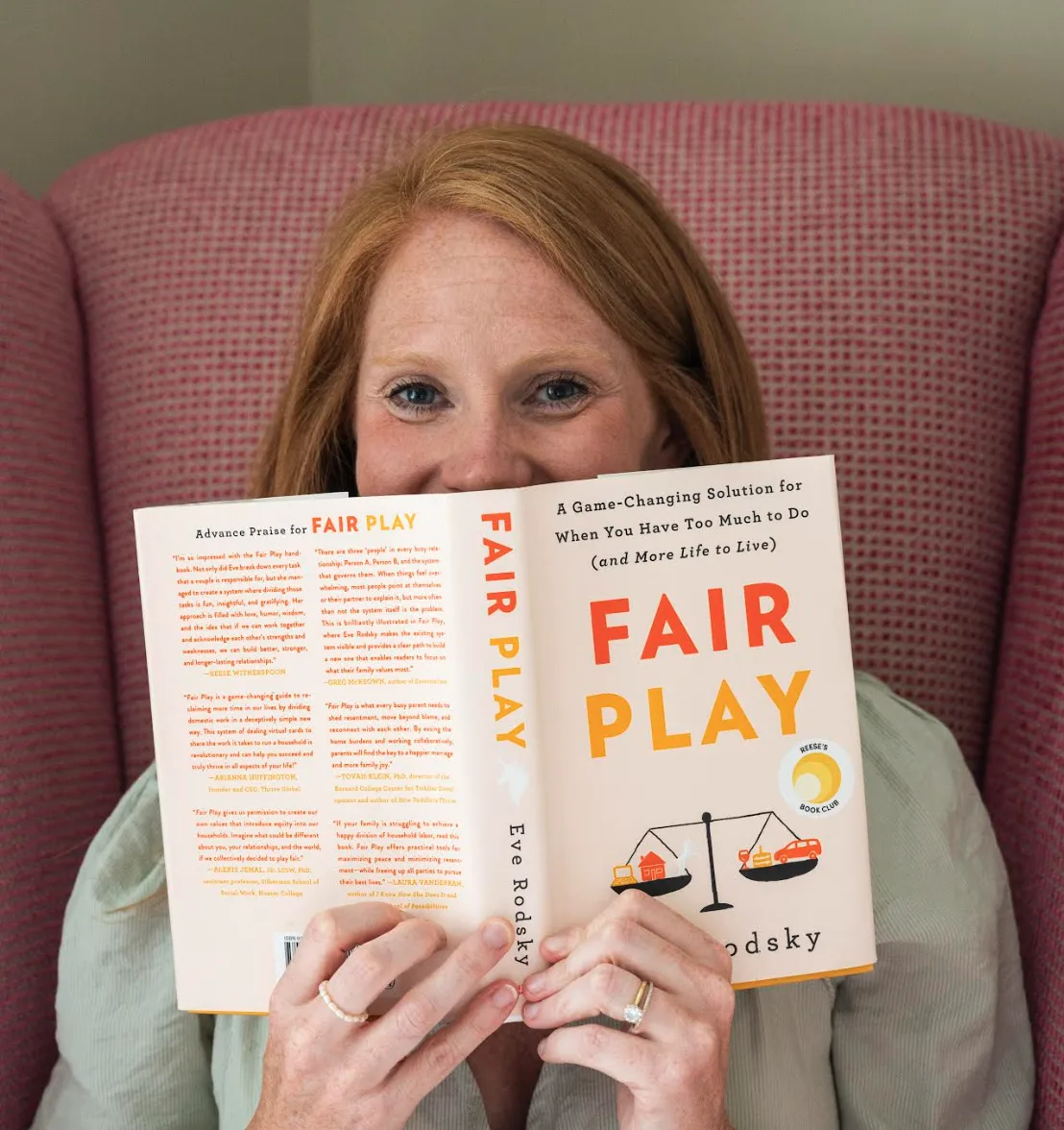 Woman with red hair holding Fair Play book by Eve Rodsky