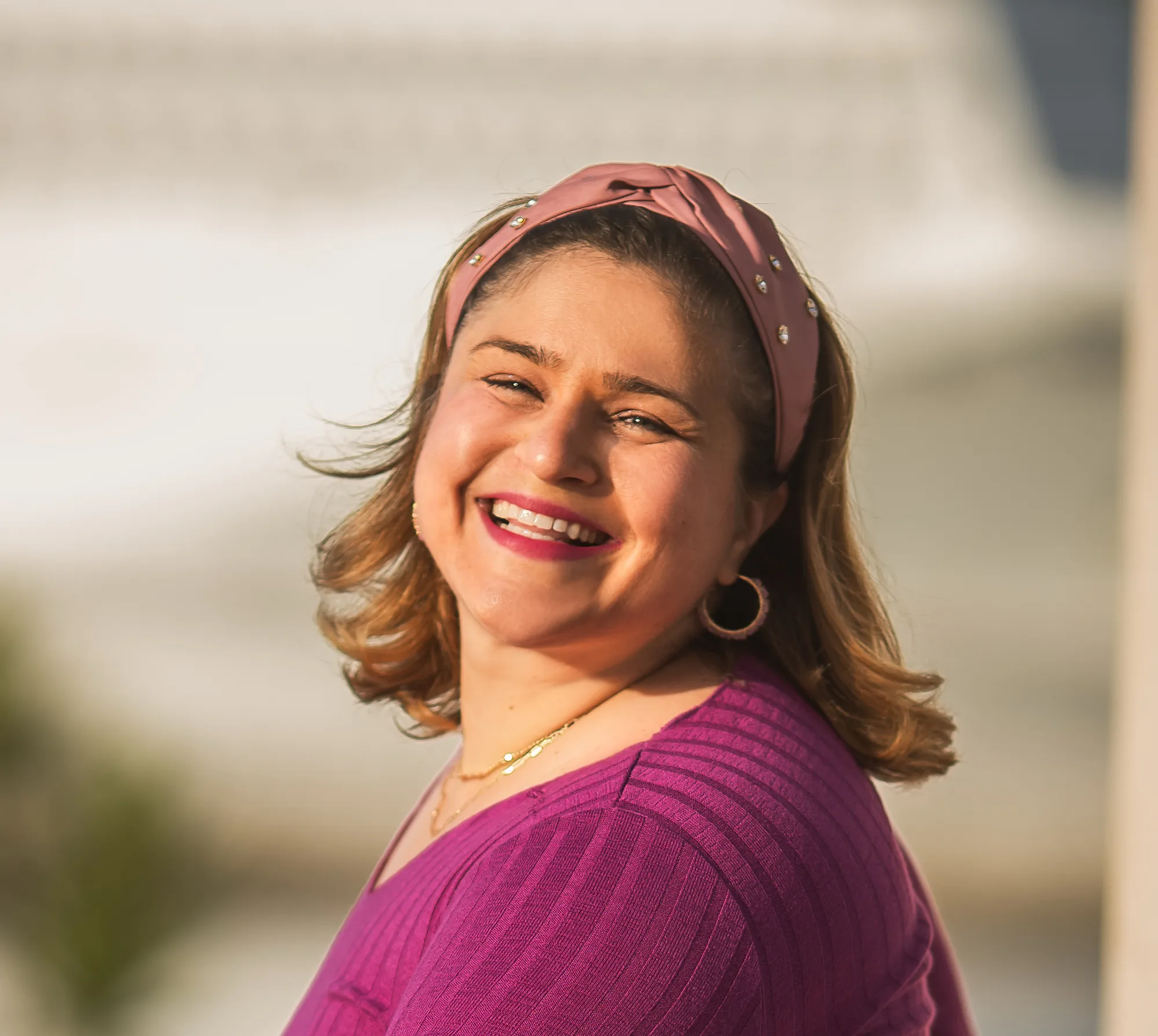 Woman wearing pink headband and purple top smiling outdoors