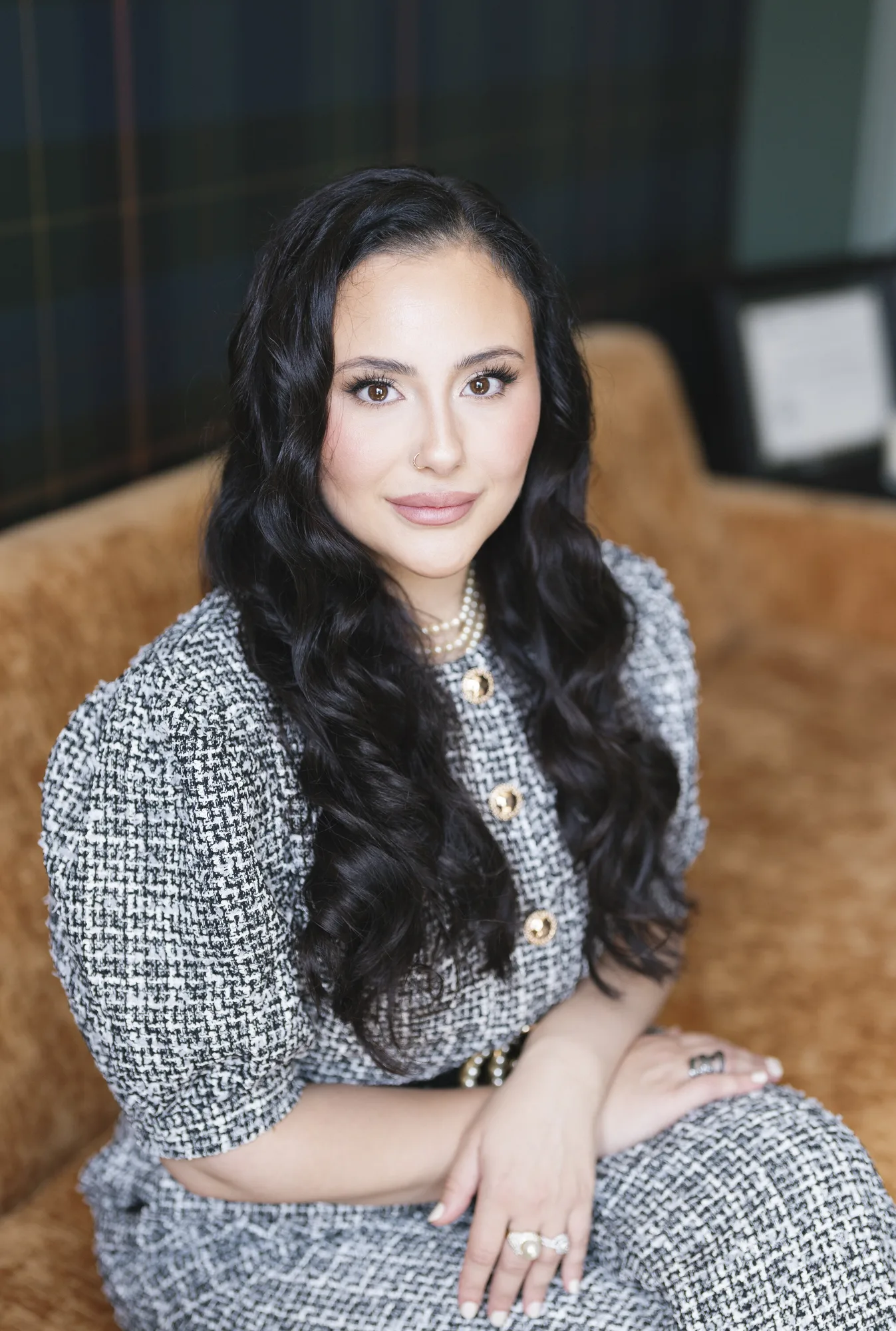 Woman with long dark hair wearing pearl necklace and tweed jacket