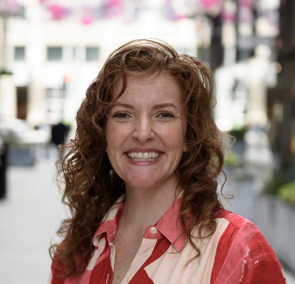 Woman with curly auburn hair smiling in coral and white striped shirt