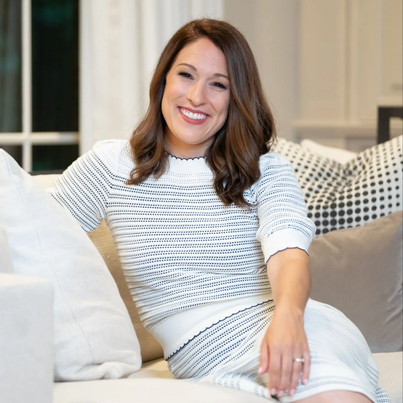 Woman in striped sweater smiling while sitting on white couch with pillows